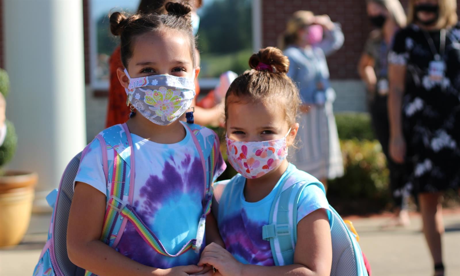Two girls smile while wearing masks
